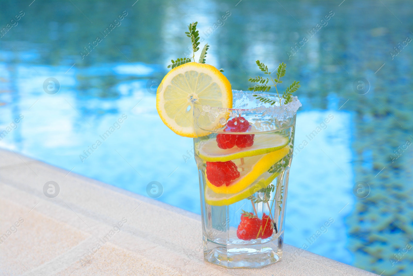 Photo of Delicious refreshing lemonade with raspberries near swimming pool