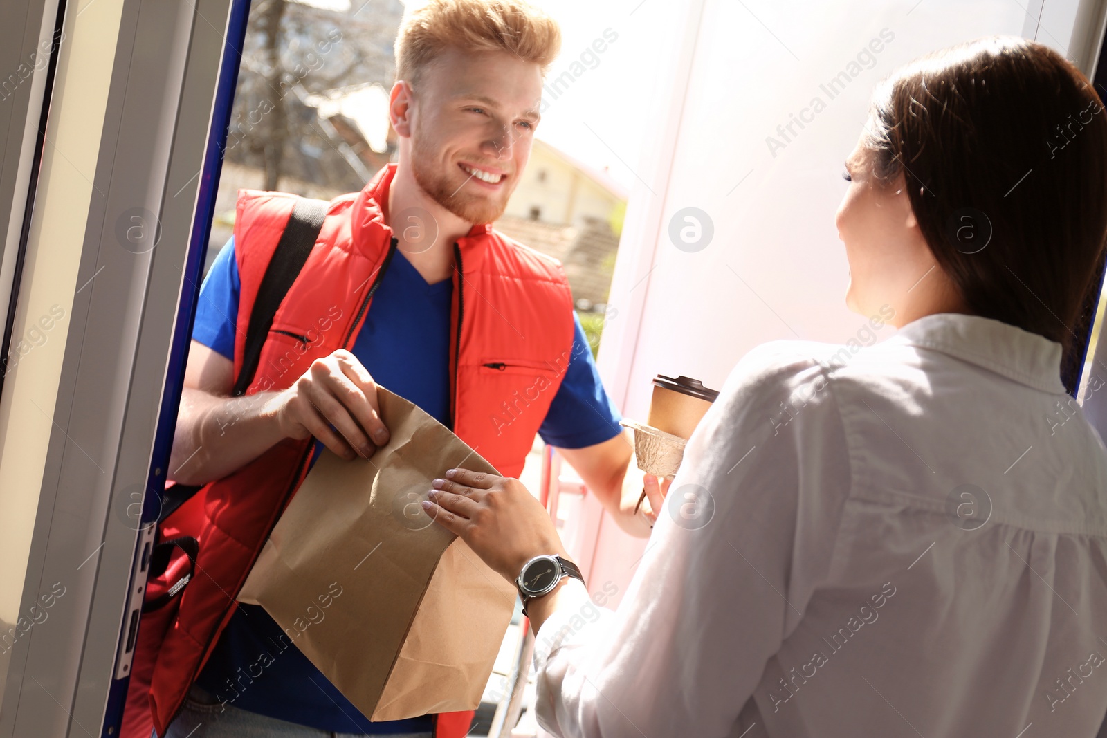 Photo of Courier giving order to young woman at open door. Food delivery service