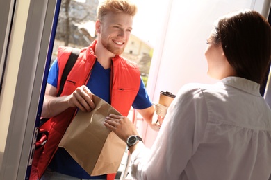 Courier giving order to young woman at open door. Food delivery service