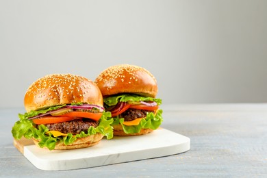 Photo of Tasty burgers on light grey wooden table, space for text. Fast food