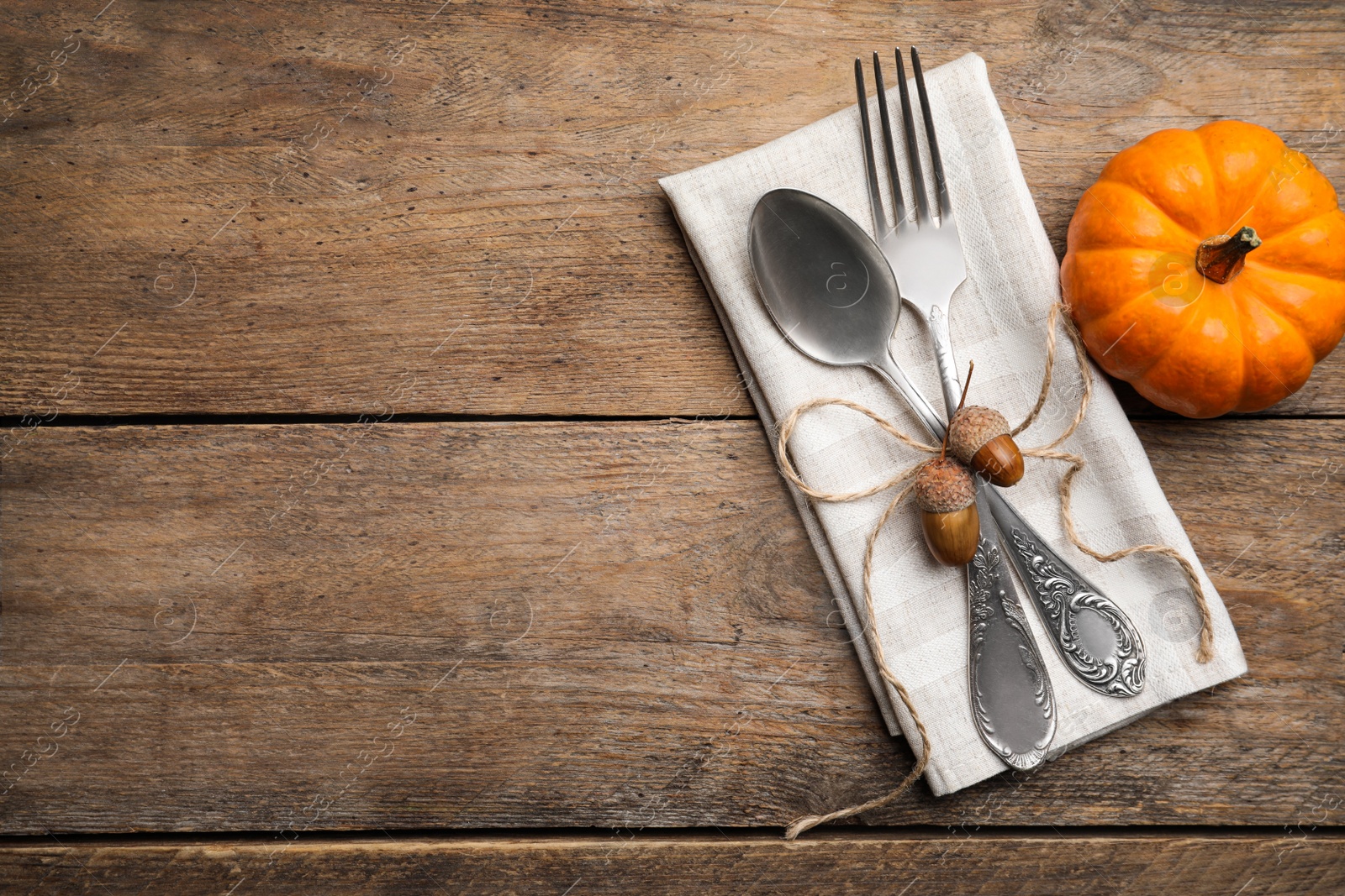 Photo of Autumn table setting, space for text. Cutlery with napkin, acorns and pumpkin on wooden background, flat lay