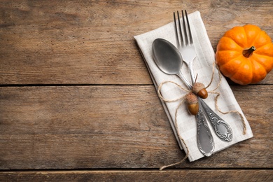 Autumn table setting, space for text. Cutlery with napkin, acorns and pumpkin on wooden background, flat lay