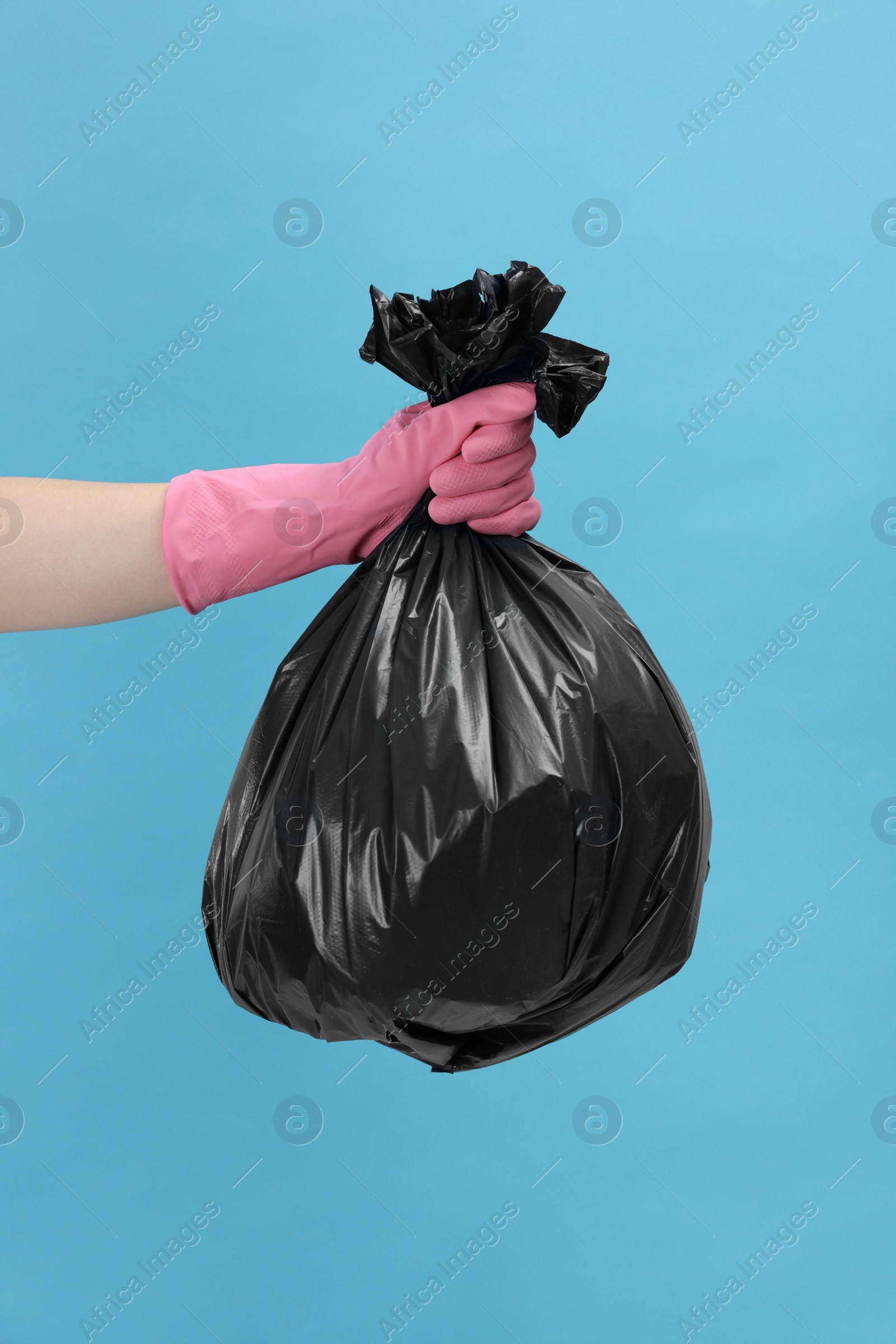 Photo of Woman holding plastic bag full of garbage on light blue background, closeup