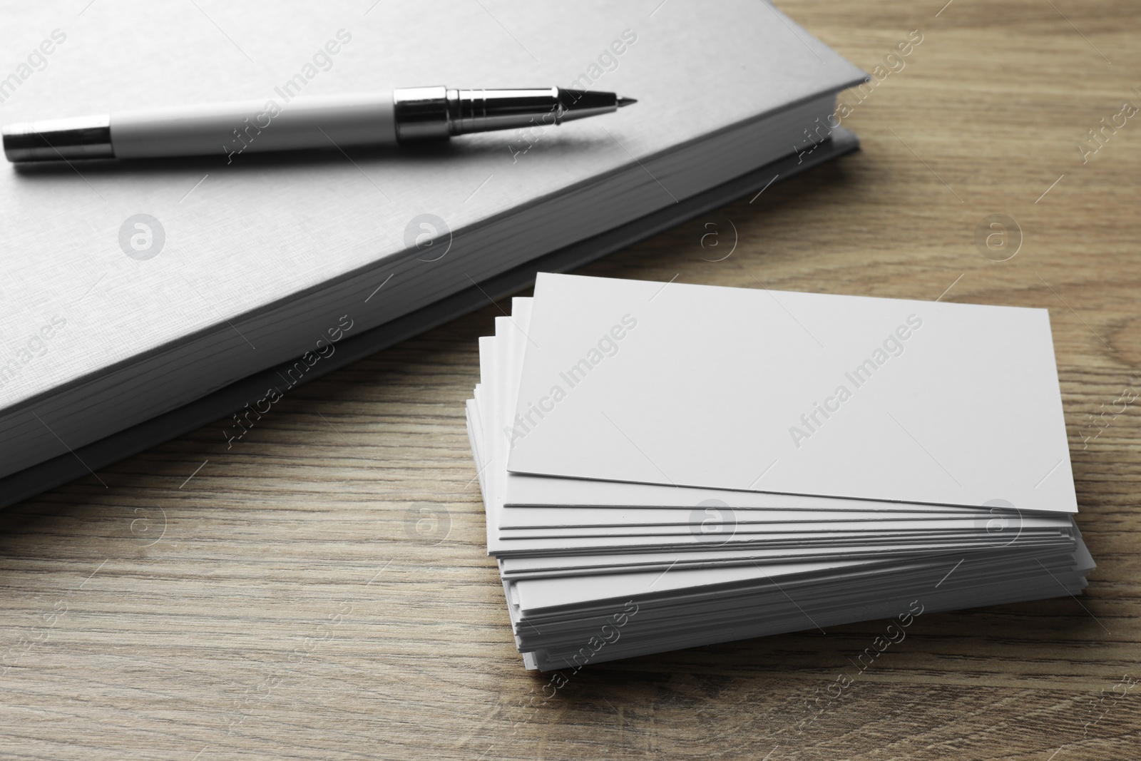 Photo of Stack of blank business cards, notebook and pen on wooden table. Mockup for design