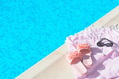 Pink blanket with slippers and sunglasses near outdoor swimming pool on sunny day, space for text