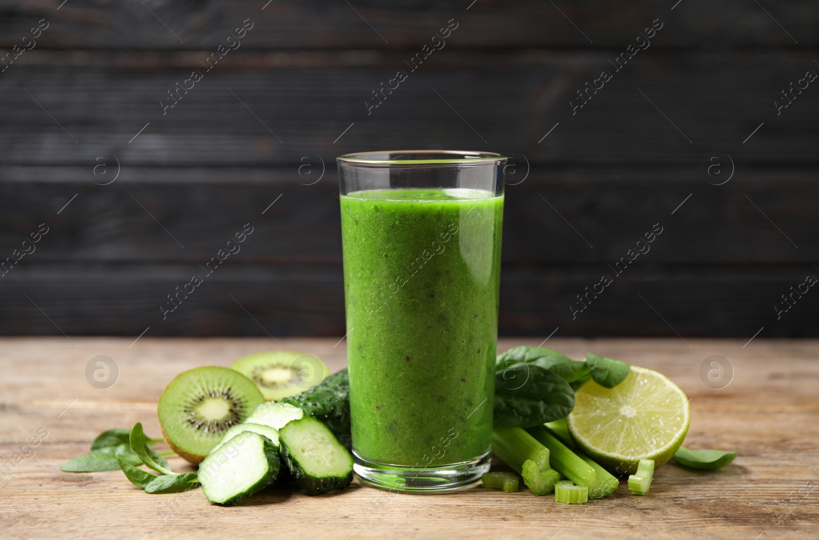 Photo of Delicious green juice and fresh ingredients on wooden table against black background