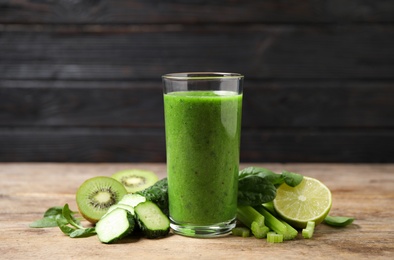 Photo of Delicious green juice and fresh ingredients on wooden table against black background