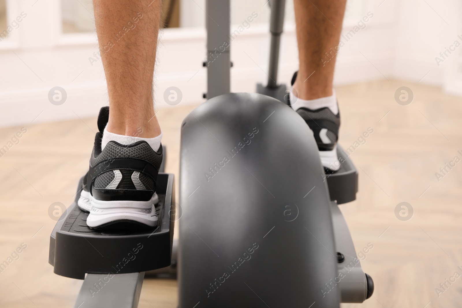 Photo of Man using modern elliptical machine indoors, closeup