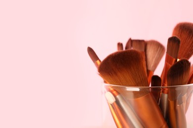 Photo of Set of professional makeup brushes on pink background, closeup. Space for text