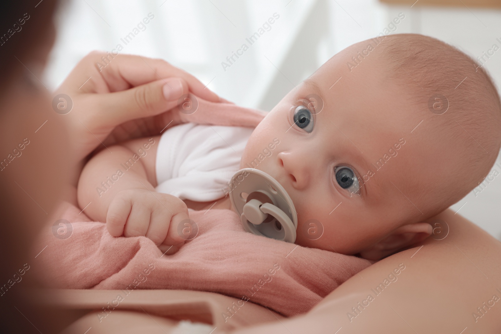 Photo of Mother holding her cute little baby with pacifier at home, closeup