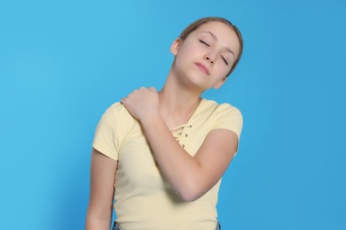 Photo of Teenage girl suffering from pain in shoulder on light blue background. Arthritis symptom