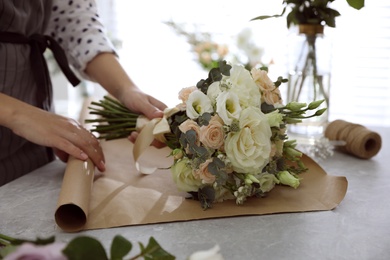 Photo of Florist making beautiful wedding bouquet at light grey marble table, closeup