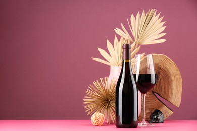 Photo of Stylish presentation of delicious red wine in bottle and glass on pink background. Space for text