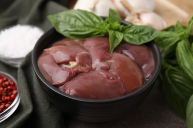 Photo of Bowl of raw chicken liver with basil on grey table, closeup