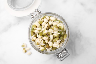 Photo of Glass jar with sprouted green mung beans on white marble table, top view