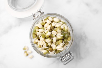 Glass jar with sprouted green mung beans on white marble table, top view