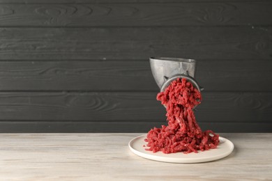 Photo of Metal meat grinder with beef mince on light wooden table. Space for text