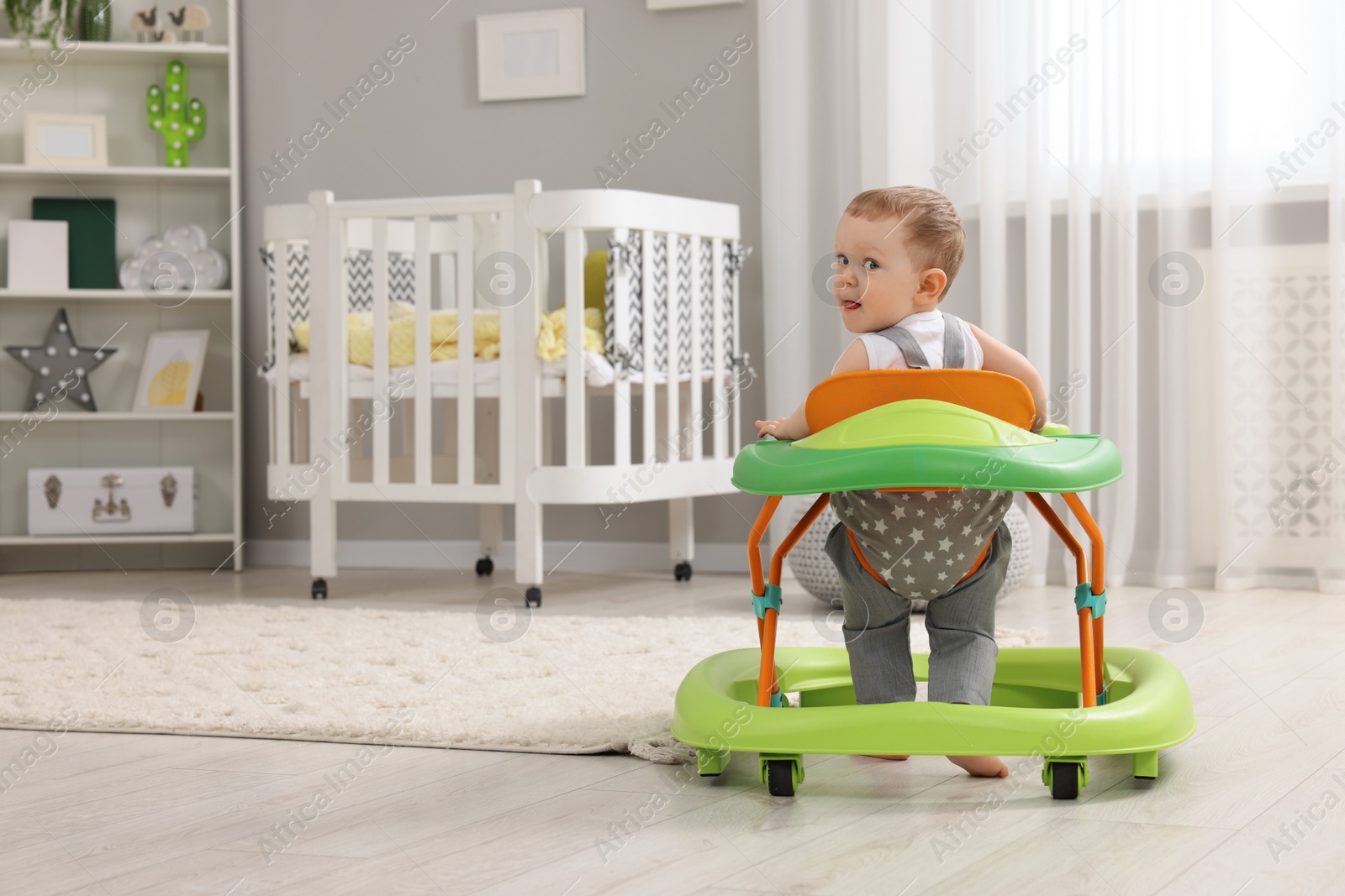 Photo of Cute baby making first steps with toy walker at home, space for text