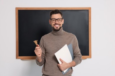 Teacher with school bell near black chalkboard indoors
