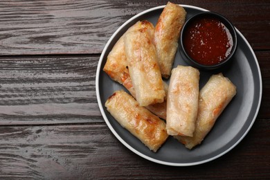 Photo of Tasty fried spring rolls and sauce on wooden table, top view. Space for text