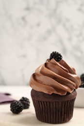 Photo of Delicious chocolate cupcake with cream and blackberries on white board, closeup. Space for text