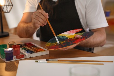 Photo of Young man with painting tools at table in artist studio, closeup