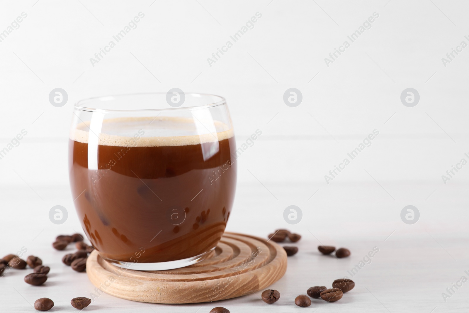 Photo of Refreshing iced coffee with milk in glass and beans on white table, space for text