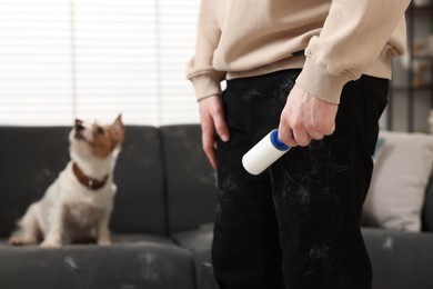 Pet shedding. Man with lint roller removing dog's hair from pants at home, closeup