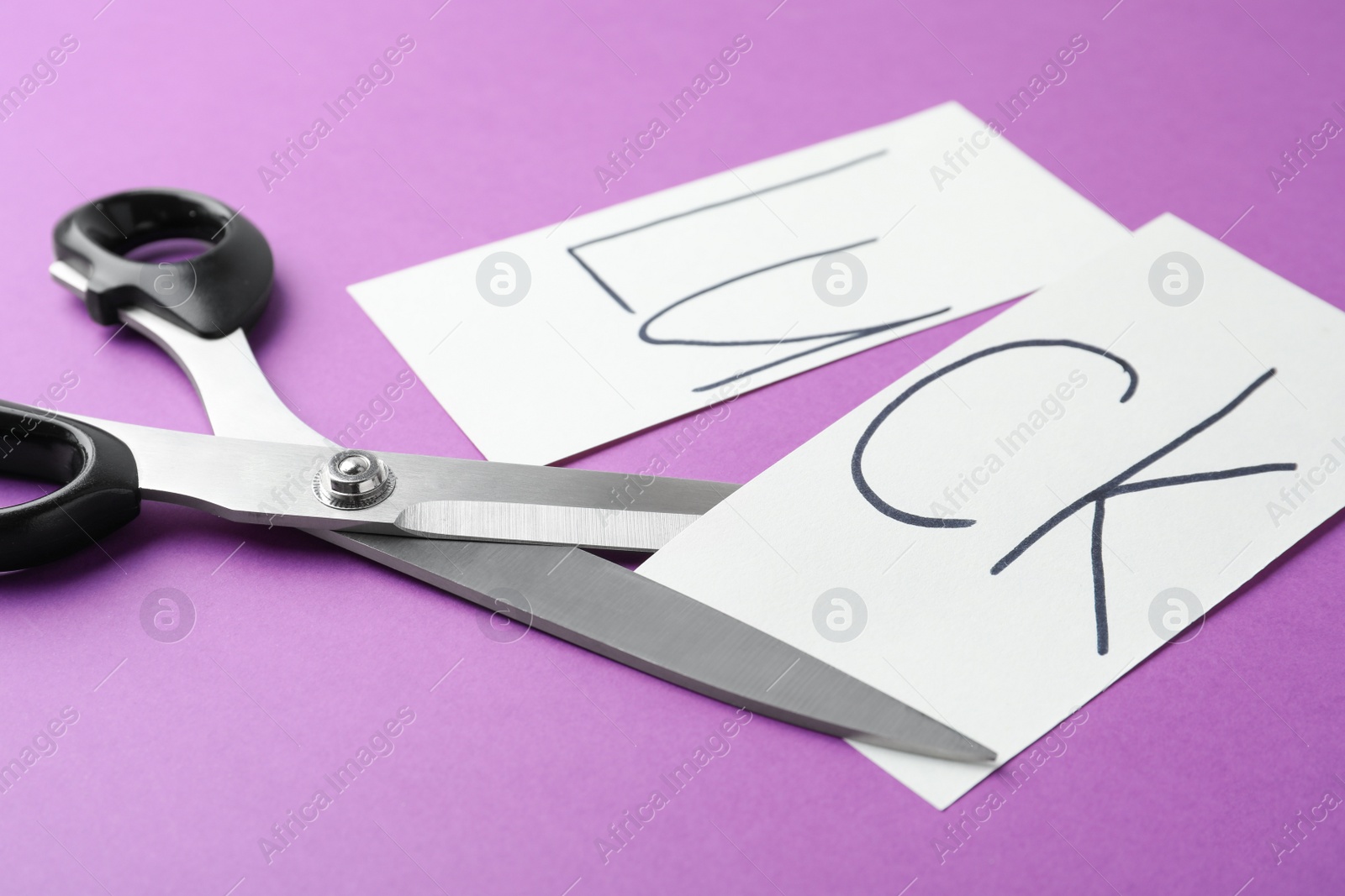 Photo of Cut paper with word LUCK and scissors on purple background, closeup