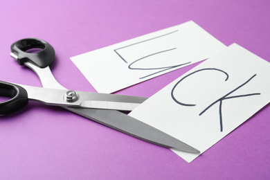 Photo of Cut paper with word LUCK and scissors on purple background, closeup