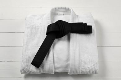 Photo of Black karate belt and white kimono on wooden background, top view