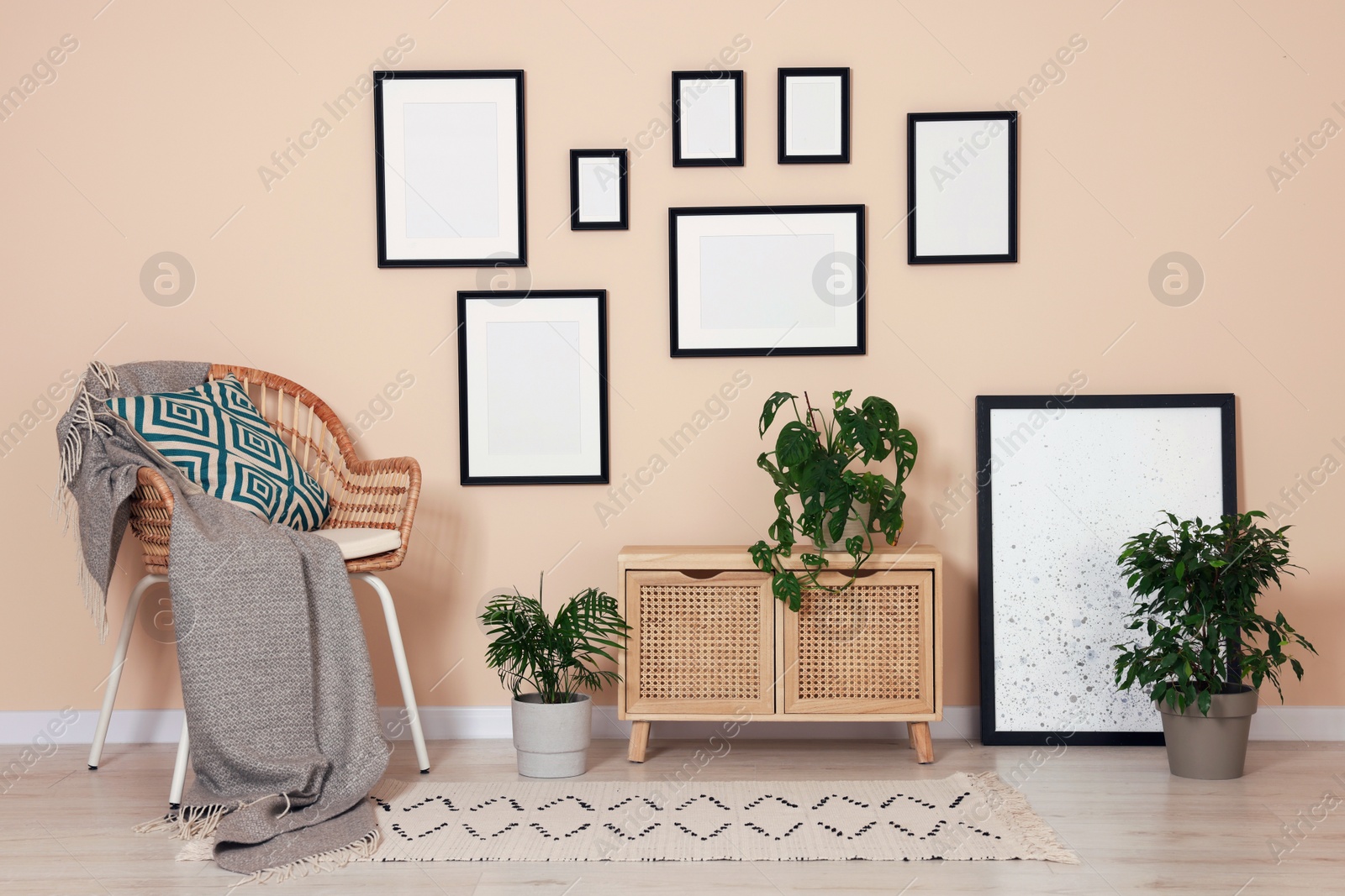 Photo of Empty frames hanging on beige wall, wooden cabinet and wicker chair indoors