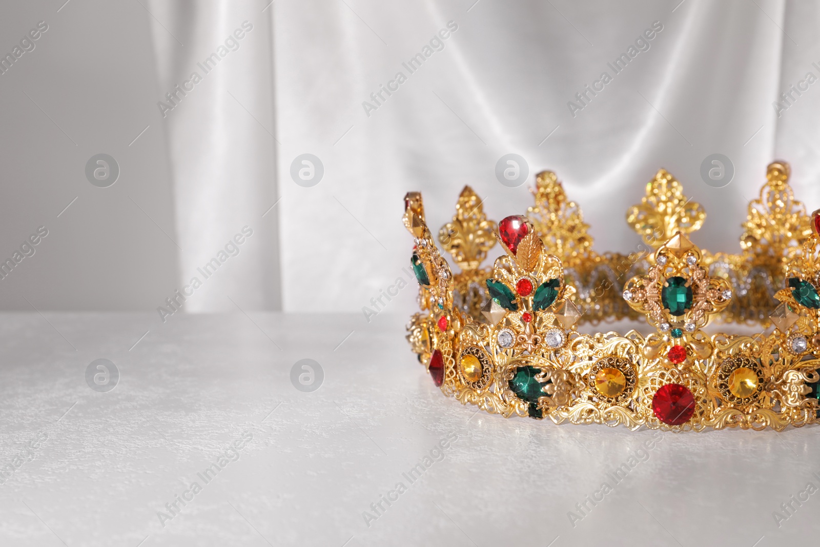 Photo of Beautiful golden crown with gems on light grey table. Space for text