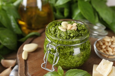 Photo of Wooden board with jar of pesto sauce and ingredients on table. Space for text