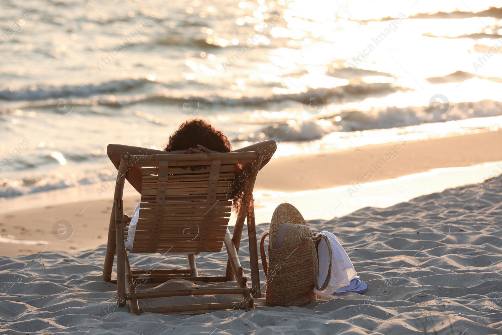 Photo of Woman resting in wooden sunbed on tropical beach at sunset