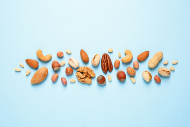 Different delicious nuts on light blue background, flat lay