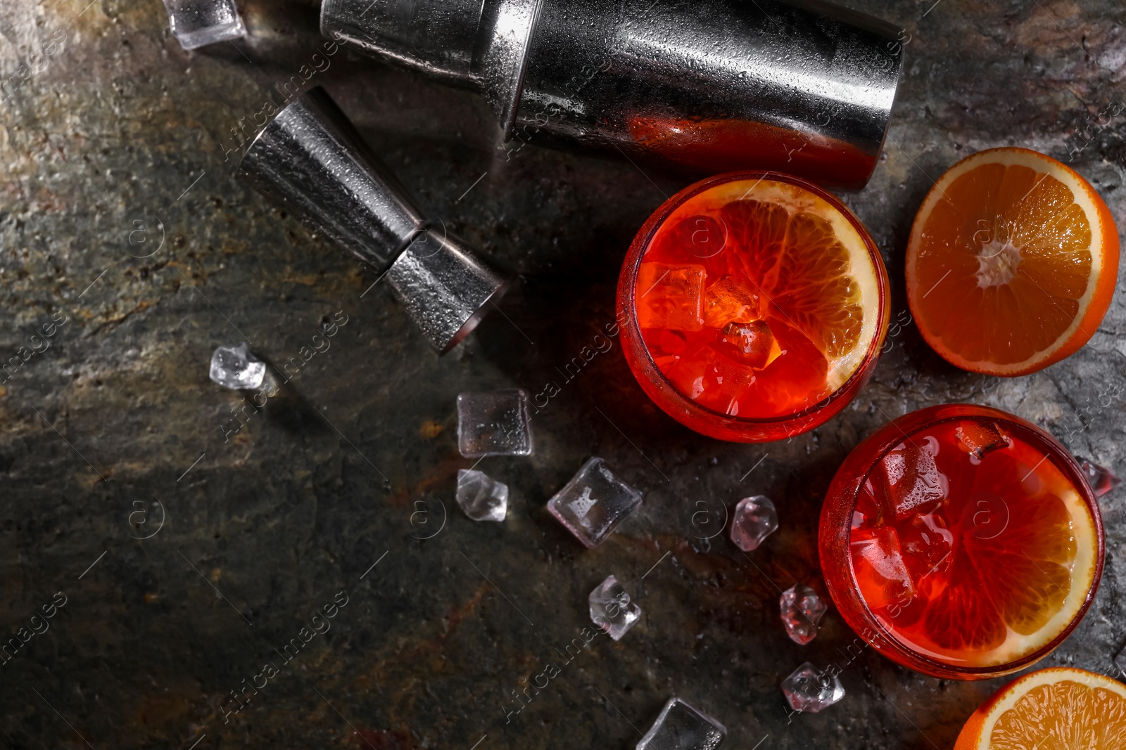 Photo of Aperol spritz cocktail, ice cubes and orange slices in glasses and shaker on grey textured table, flat lay. Space for text