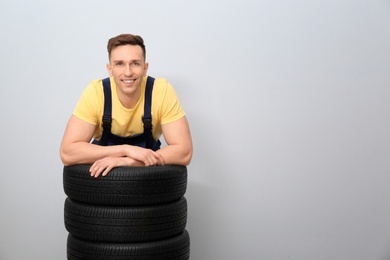 Male mechanic with car tires on light background