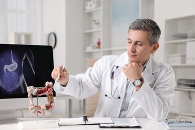 Gastroenterologist showing anatomical model of large intestine at table in clinic