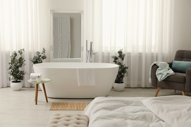 Stylish light apartment interior with white bathtub and bed