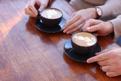 Photo of Couple with cups of aromatic coffee at wooden table, closeup