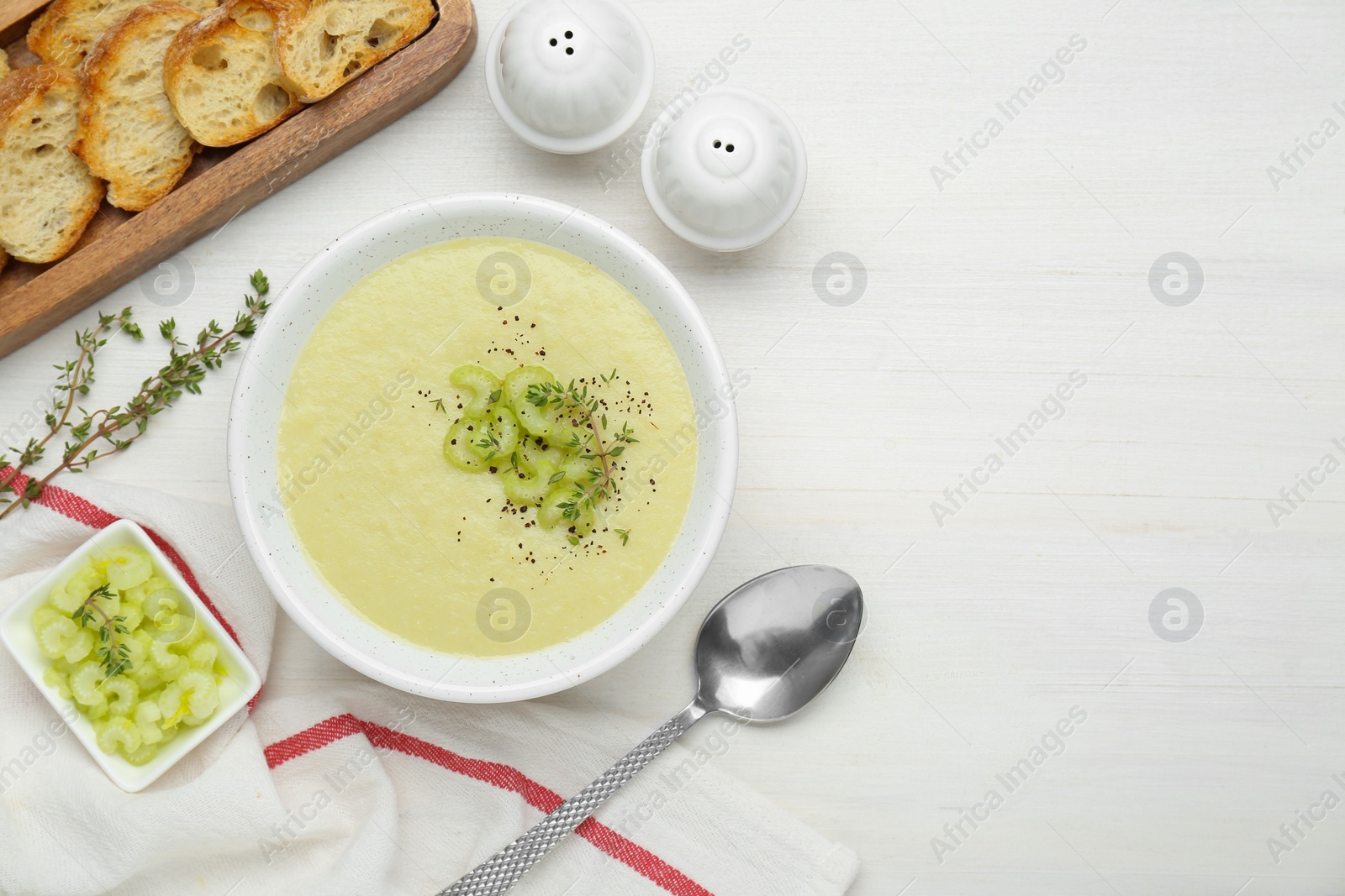 Photo of Bowl of delicious celery soup served on white wooden table, flat lay. Space for text