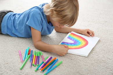 Photo of Little boy drawing rainbow on floor indoors. Stay at home concept