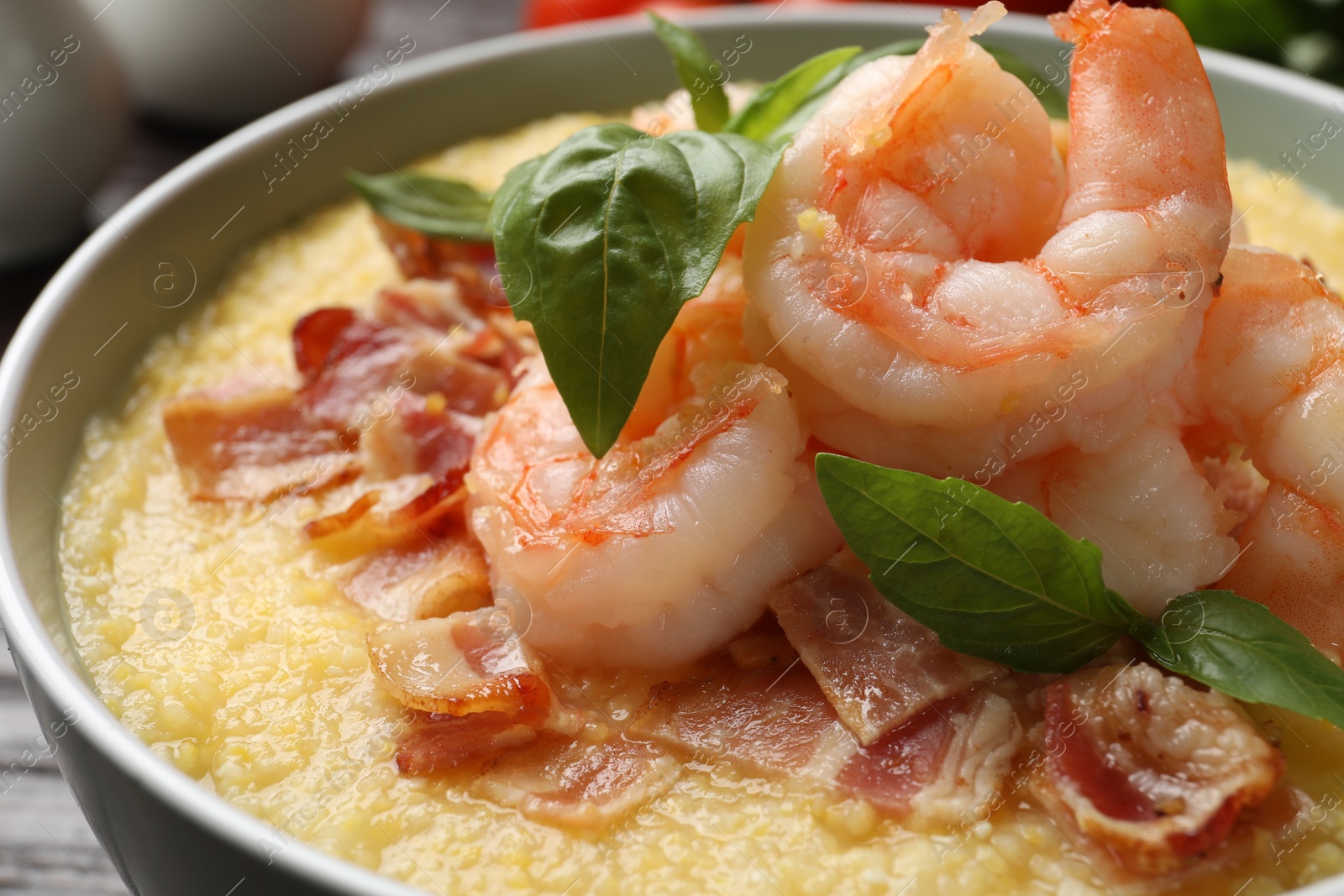 Photo of Fresh tasty shrimps, bacon, grits and basil in bowl on table, closeup