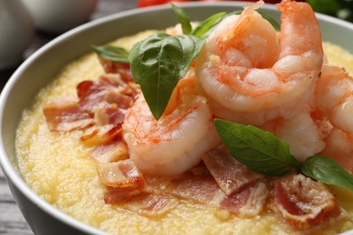 Photo of Fresh tasty shrimps, bacon, grits and basil in bowl on table, closeup