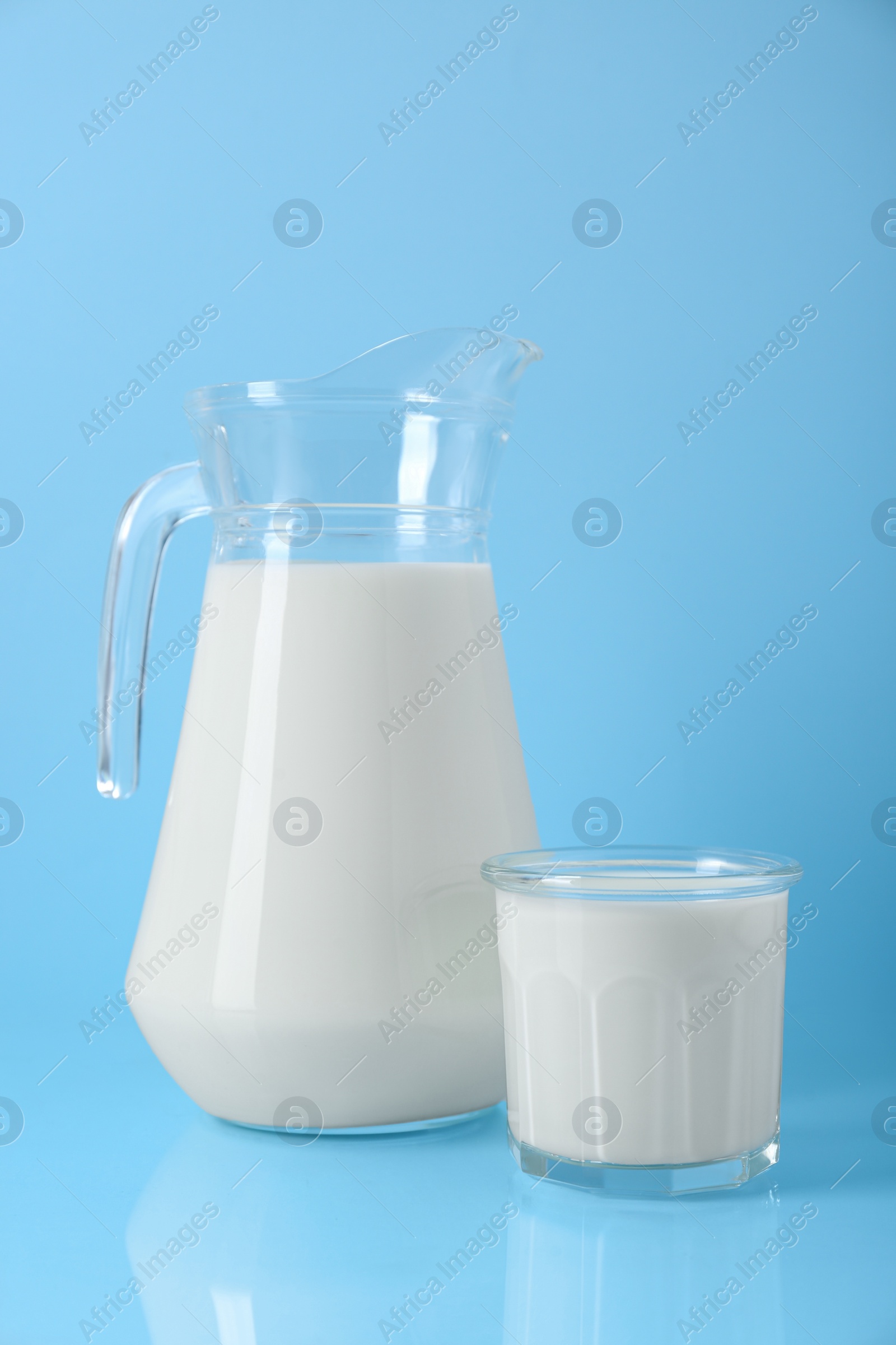 Photo of Jug and glass of fresh milk on light blue background
