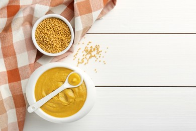 Photo of Tasty mustard sauce and dry seeds on white wooden table, flat lay. Space for text