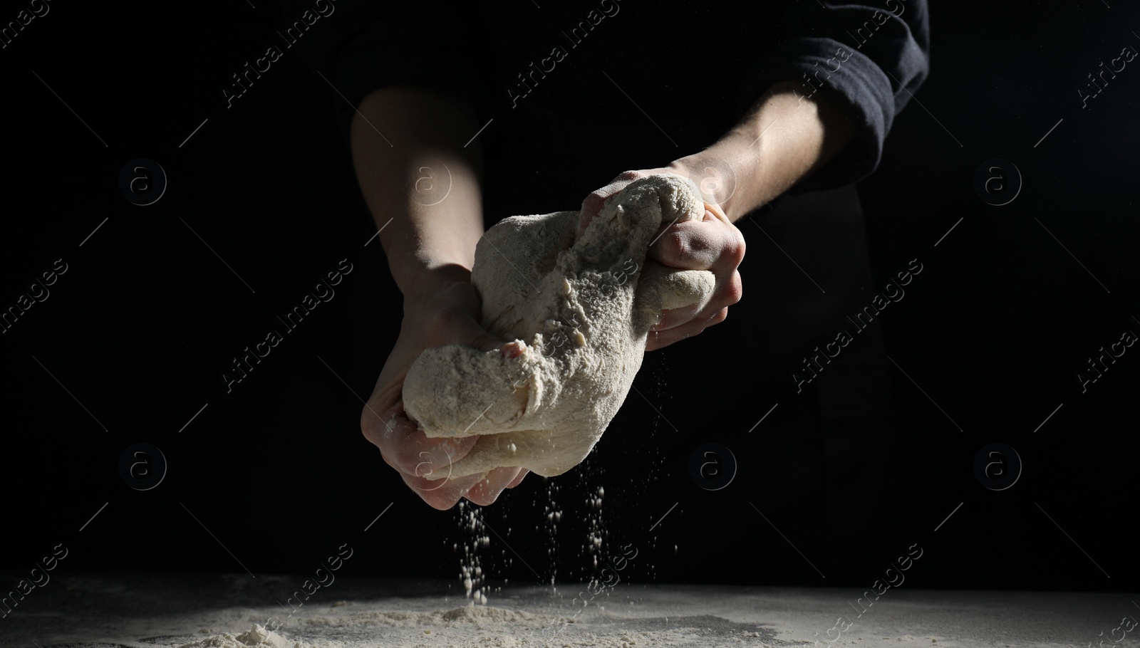 Photo of Making bread. Woman kneading dough at table on dark background, closeup