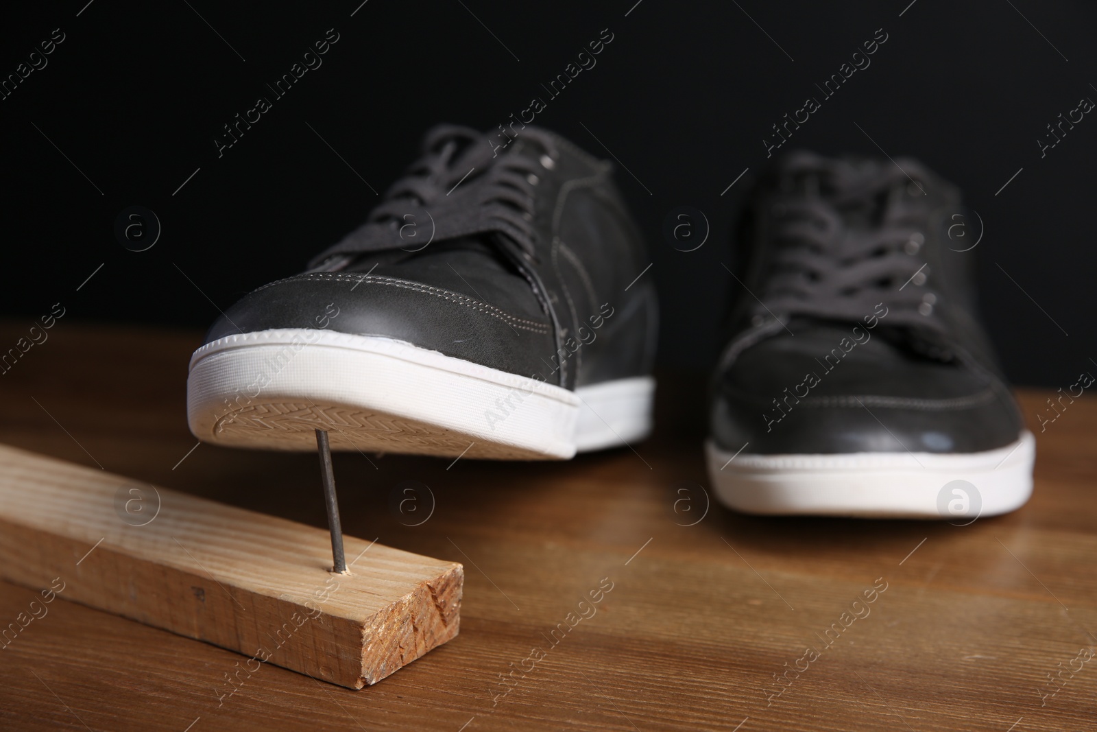 Photo of Metal nail in wooden plank and shoes on table
