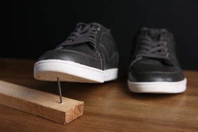 Photo of Metal nail in wooden plank and shoes on table
